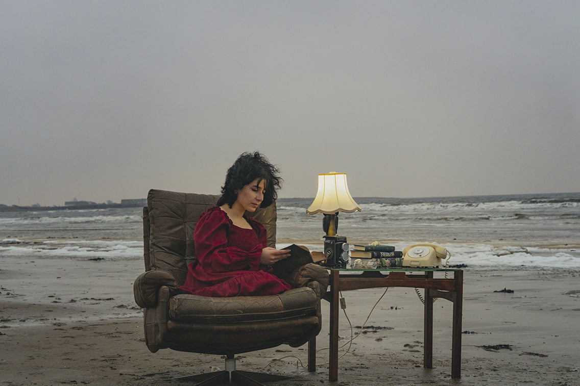 Kvinna som läser i fåtölj på stranden.
