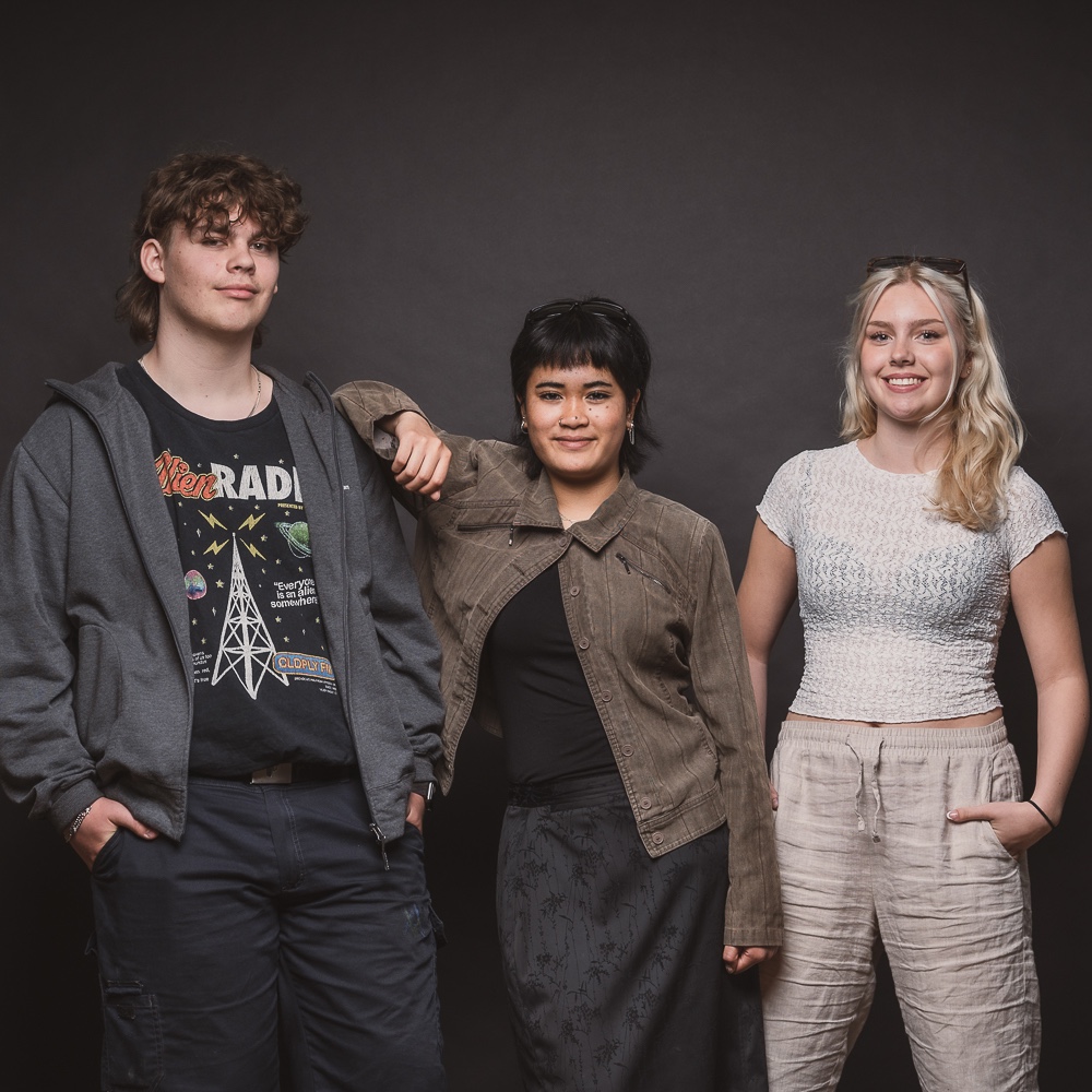 Tre elever i en fotostudio poserar framför kameran